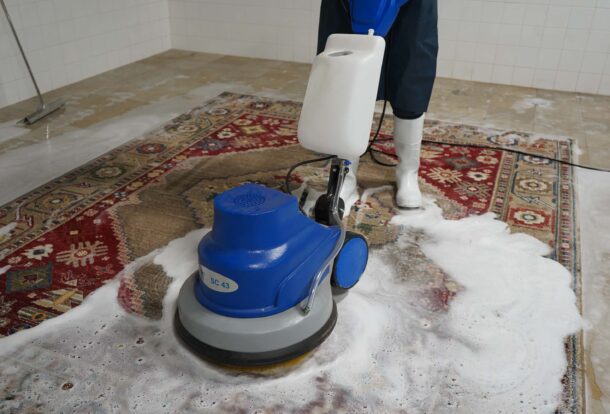 Deep cleaning of an Oriental rug using a rotary machine and foam shampoo, performed by a professional rug cleaner in a tiled cleaning facility