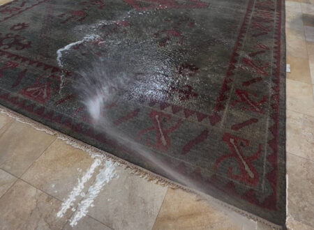 Professional pre-wash cleaning process for an Oriental rug, showing deep cleaning techniques with water spray on a tiled surface.