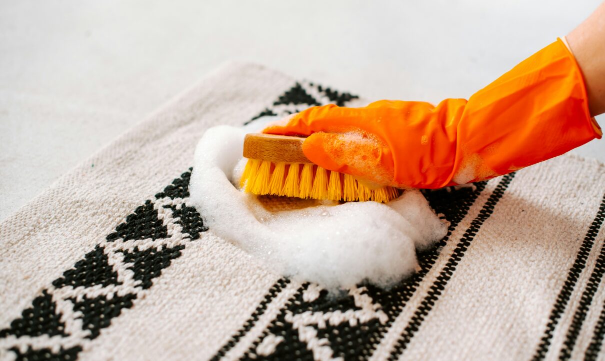 Gloved hand scrubbing a soapy stain on a patterned rug with a brush – deep stain removal by RugGuys professional cleaning service