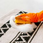 Gloved hand scrubbing a soapy stain on a patterned rug with a brush – deep stain removal by RugGuys professional cleaning service