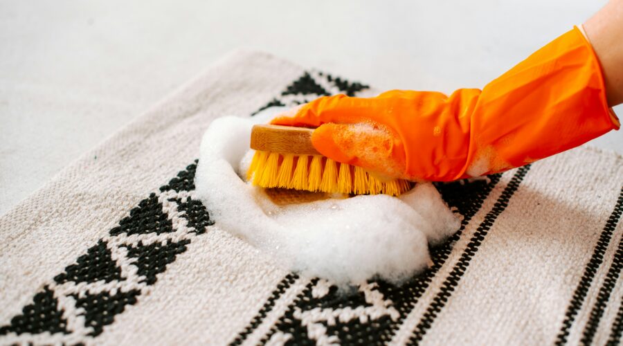 Gloved hand scrubbing a soapy stain on a patterned rug with a brush – deep stain removal by RugGuys professional cleaning service
