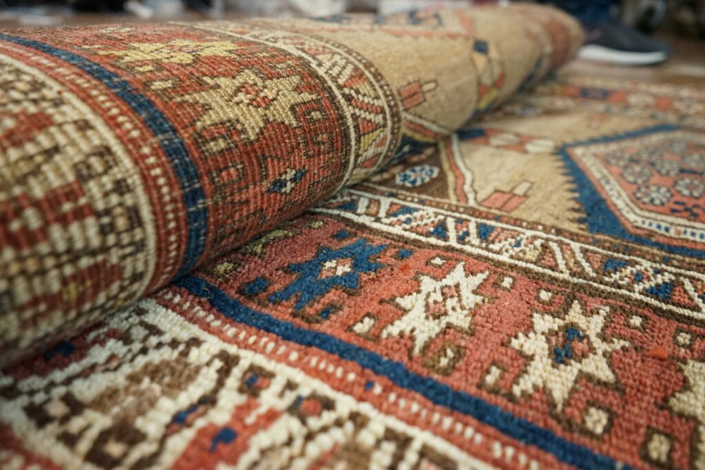 Close-up of a rolled vintage Oriental rug with red, blue, and cream geometric patterns, ideal for professional rug cleaning, repair, and restoration services in Dallas-Fort Worth
