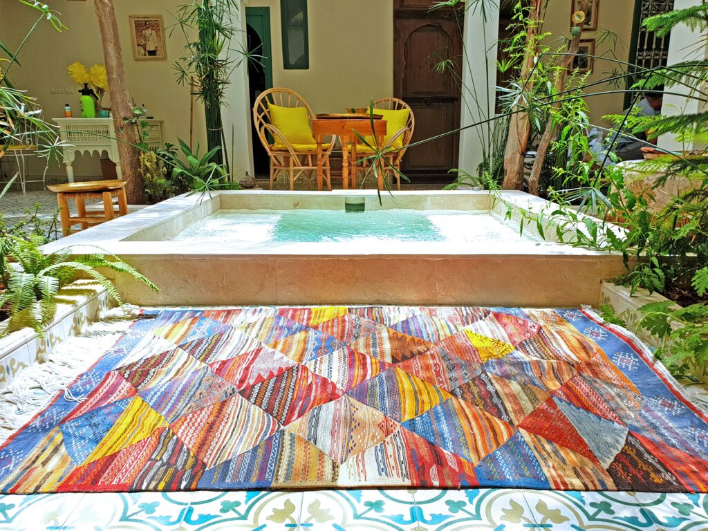 Colorful handmade Berber Moroccan rug with diamond patchwork patterns placed near an indoor pool and wicker chairs – RugGuys rug cleaning and care in Dallas-Fort Worth