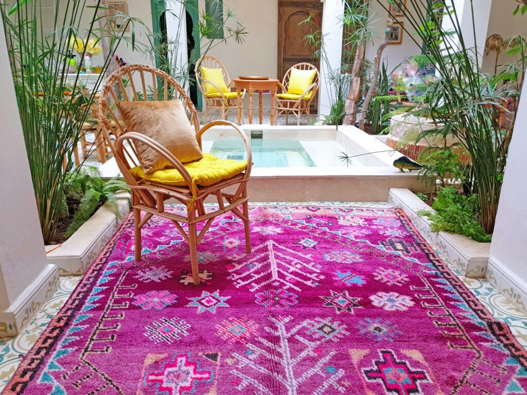 Bright pink Moroccan handmade rug with geometric patterns placed in a tropical indoor patio with wicker chairs, plants, and tiled flooring – RugGuys rug cleaning DFW