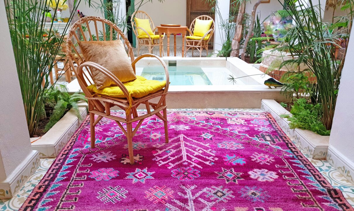 Bright pink Moroccan handmade rug with geometric patterns placed in a tropical indoor patio with wicker chairs, plants, and tiled flooring – RugGuys rug cleaning DFW