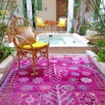 Bright pink Moroccan handmade rug with geometric patterns placed in a tropical indoor patio with wicker chairs, plants, and tiled flooring – RugGuys rug cleaning DFW