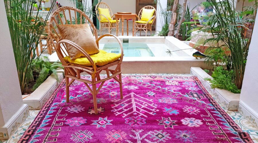 Bright pink Moroccan handmade rug with geometric patterns placed in a tropical indoor patio with wicker chairs, plants, and tiled flooring – RugGuys rug cleaning DFW