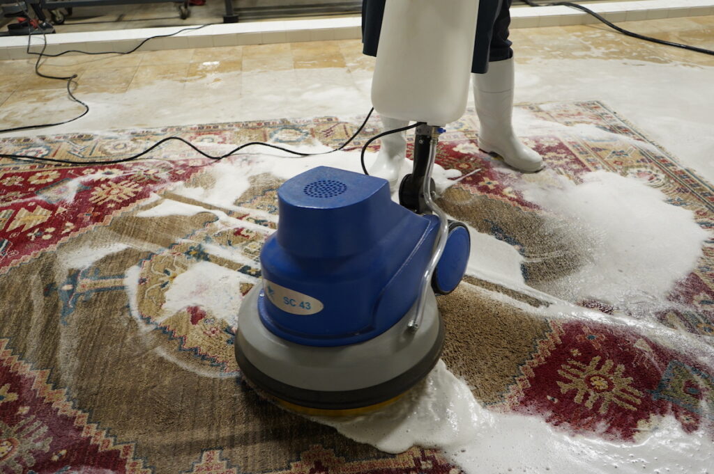 Professional rug cleaning process with a machine scrubber on a colorful patterned rug, applying cleaning foam.